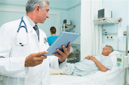 simsearch:6109-06196339,k - Doctor using a tactile tablet while looking at a patient in a bed ward Stock Photo - Premium Royalty-Free, Code: 6109-06196285