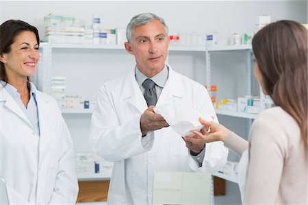 simsearch:6109-06196243,k - Smiling pharmacist with a colleague in front of a female client Stock Photo - Premium Royalty-Free, Code: 6109-06196203