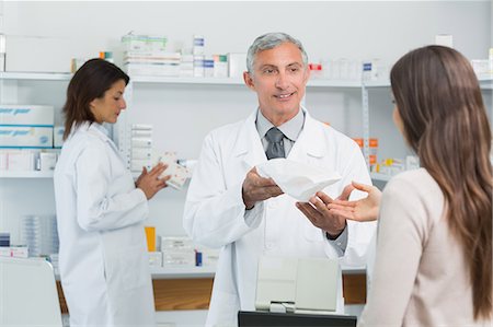 simsearch:6109-06196216,k - Smiling pharmacist standing giving medicine to a client Stock Photo - Premium Royalty-Free, Code: 6109-06196206
