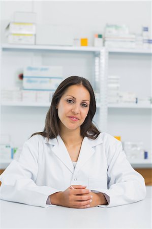 simsearch:6109-06196216,k - Smiling female pharmacist joining her hands on the counter of a pharmacy Stock Photo - Premium Royalty-Free, Code: 6109-06196237