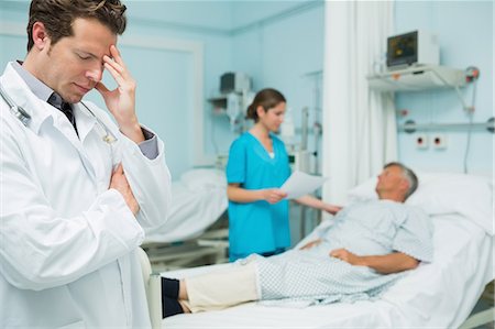 récupérer - Thoughtful male doctor with standing in the foreground of a room Foto de stock - Sin royalties Premium, Código: 6109-06196365