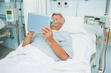 Homme patient allongé sur un lit avec un masque tout en maintenant une tablette tactile Photographie de stock - Premium Libres de Droits, Code: 6109-06196374