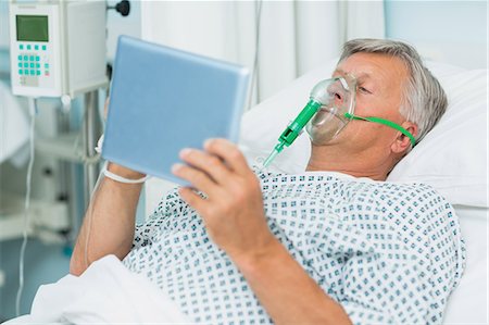 Senior patient lying on a bed with a mask while holding a tactile tablet Foto de stock - Sin royalties Premium, Código: 6109-06196375