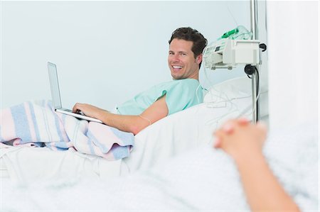stériliser - Concentrer le tir d'un patient mâle souriant taper sur un ordinateur portable en position couchée sur un lit Photographie de stock - Premium Libres de Droits, Code: 6109-06196309