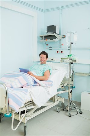 simsearch:6109-06196316,k - Joyful male patient holding a tactile tablet while lying on a bed Foto de stock - Sin royalties Premium, Código: 6109-06196328