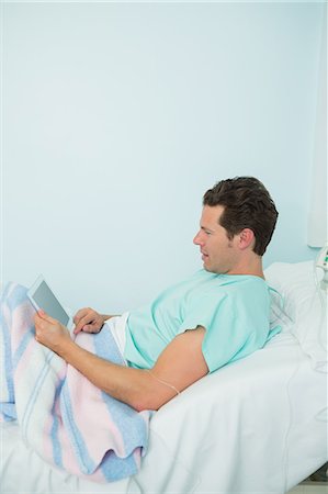 Patient touching a tactile tablet while lying on a bed Stock Photo - Premium Royalty-Free, Code: 6109-06196332