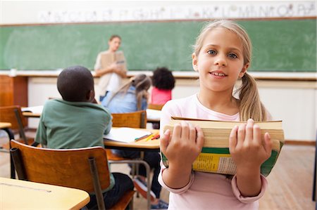 small girl photo - Schoolgirl holding pile of books in classroom Stock Photo - Premium Royalty-Free, Code: 6109-06196477