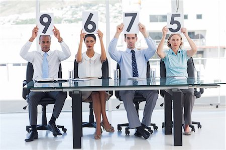 executive looking at camera on desk - Sitting panel of judges showing marks Stock Photo - Premium Royalty-Free, Code: 6109-06781342