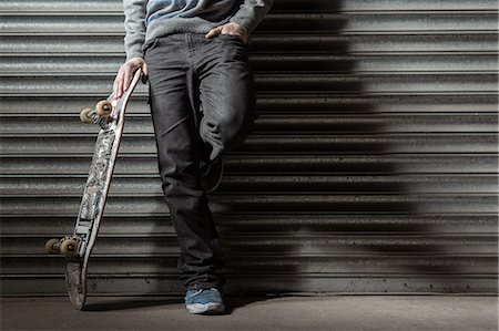 Skater leaning against metal shutters Stock Photo - Premium Royalty-Free, Code: 6109-06781443