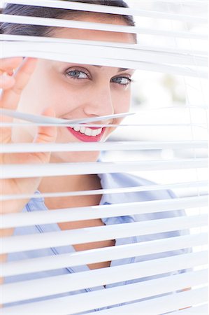 Attractive businesswoman looking through a venetian blind Stock Photo - Premium Royalty-Free, Code: 6109-06781743