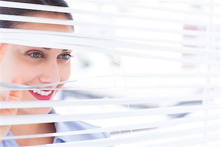 Beautiful businesswoman peeking through venetian blind Stock Photo - Premium Royalty-Free, Code: 6109-06781742