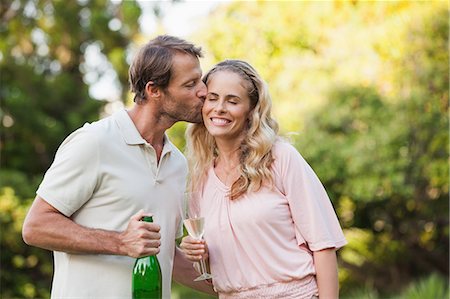 Man kissing his wife while holding champagne bottle outside on a summers day Photographie de stock - Premium Libres de Droits, Code: 6109-07497014