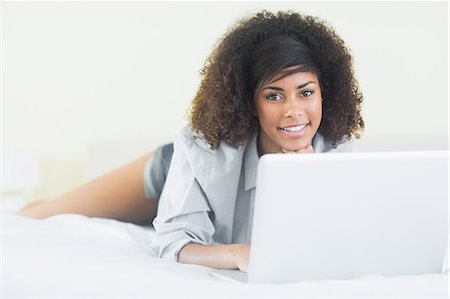 simsearch:6109-08581996,k - Pretty smiling brunette lying on bed using laptop in bright bedroom Fotografie stock - Premium Royalty-Free, Codice: 6109-07497244