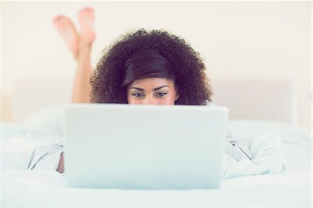 Pretty brunette lying on bed using laptop in bright bedroom Foto de stock - Royalty Free Premium, Número: 6109-07497245