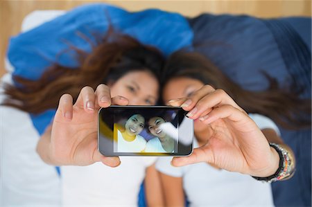 Two happy young sisters taking a picture of themselves while lying on a bed Stock Photo - Premium Royalty-Free, Code: 6109-07497211