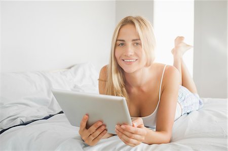 simsearch:6109-07497402,k - Pretty smiling blonde using digital tablet on her bed at home in bedroom Foto de stock - Sin royalties Premium, Código: 6109-07497388