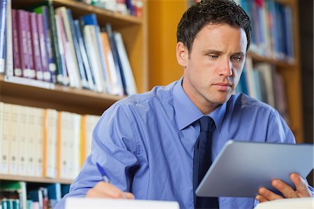 simsearch:6109-07497468,k - Frowning librarian sitting at desk using tablet in library in a college Stockbilder - Premium RF Lizenzfrei, Bildnummer: 6109-07497468