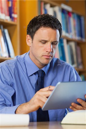 simsearch:6109-07497575,k - Concentrating librarian sitting at desk using tablet in library in a college Foto de stock - Sin royalties Premium, Código: 6109-07497470