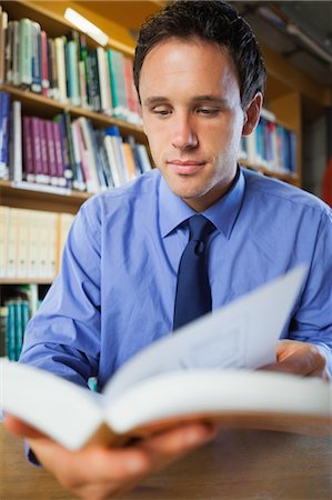 simsearch:6109-07497725,k - Attractive librarian sitting at desk reading a book in library in a college Stock Photo - Premium Royalty-Free, Code: 6109-07497476