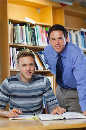simsearch:6109-07497720,k - Smiling lecturer and student looking at camera in library in a college Stock Photo - Premium Royalty-Free, Code: 6109-07497495