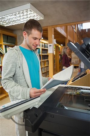 simsearch:6109-07497515,k - Happy good looking student standing next to photocopier in library in a college Photographie de stock - Premium Libres de Droits, Code: 6109-07497514