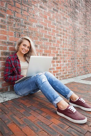 simsearch:6109-07497517,k - Happy gorgeous student leaning against wall using laptop on college campus Foto de stock - Royalty Free Premium, Número: 6109-07497519