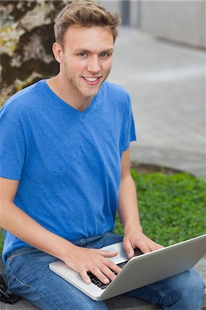 simsearch:6109-07497517,k - Cheerful handsome student sitting on wall using laptop on college campus Foto de stock - Royalty Free Premium, Número: 6109-07497529