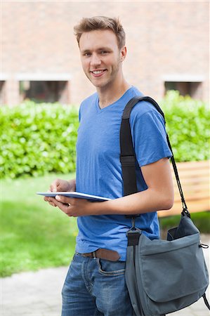 Happy handsome student holding tablet and standing on college campus Stock Photo - Premium Royalty-Free, Code: 6109-07497530