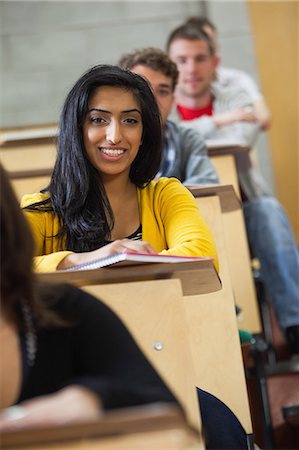 simsearch:6109-07497603,k - Smiling indian student taking notes in a lecture hall in college Foto de stock - Sin royalties Premium, Código: 6109-07497659