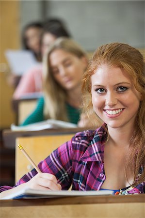 simsearch:6109-07497640,k - Smiling red head student taking notes in a lecture hall in college Photographie de stock - Premium Libres de Droits, Code: 6109-07497661