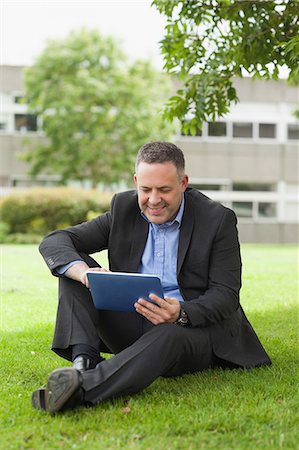 simsearch:6109-07497695,k - Happy lecturer using his tablet pc sitting outside on campus at the university Foto de stock - Sin royalties Premium, Código: 6109-07497694