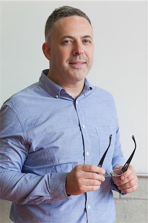 Smiling lecturer standing in his classroom holding his glasses in college Stock Photo - Premium Royalty-Free, Code: 6109-07497630