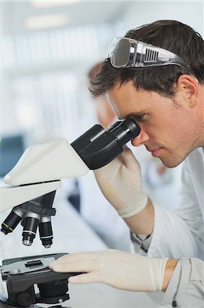 simsearch:6109-08389507,k - Attractive calm scientist looking through a microscope standing in a laboratory Stock Photo - Premium Royalty-Free, Code: 6109-07497746