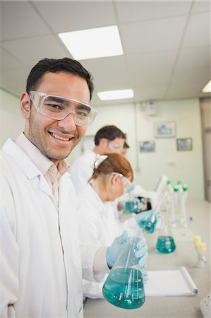 simsearch:6109-07497806,k - Young male scientist holding an erlenmeyer flask standing in a laboratory smiling at camera Fotografie stock - Premium Royalty-Free, Codice: 6109-07497772