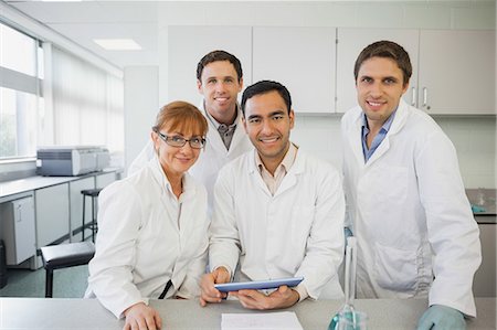 Some scientists standing behind a desk in the laboratory holding a tablet while smiling at camera Foto de stock - Sin royalties Premium, Código: 6109-07497784