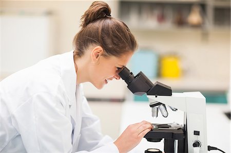 simsearch:6109-07497797,k - Smiling brunette student looking through microscope in lab at college Fotografie stock - Premium Royalty-Free, Codice: 6109-07497791