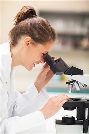 simsearch:6109-07497797,k - Cheerful brunette student looking through microscope in lab at college Fotografie stock - Premium Royalty-Free, Codice: 6109-07497792