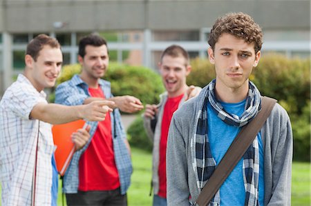 Lonely student being bullied by group of brutish classmates looking hopelessly at the camera at the university Stock Photo - Premium Royalty-Free, Code: 6109-07497708