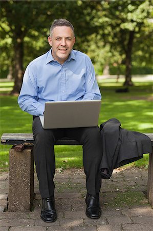 simsearch:6109-07497695,k - Smiling lecturer sitting on bench using laptop on campus at the university Foto de stock - Sin royalties Premium, Código: 6109-07497710