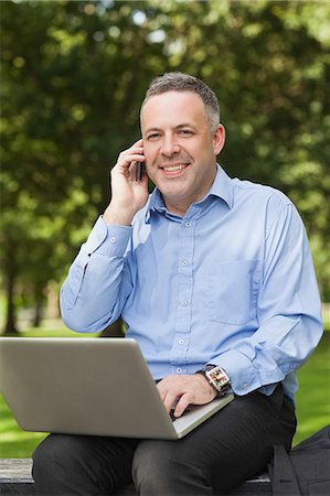 simsearch:6109-07497720,k - Laughing professor talking on phone while sitting on bench using laptop on campus at the university Stock Photo - Premium Royalty-Free, Code: 6109-07497714