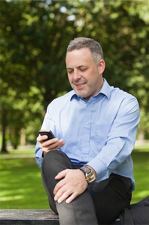simsearch:6109-07497725,k - Happy professor texting on phone while sitting on bench on campus at the university Stock Photo - Premium Royalty-Free, Code: 6109-07497715