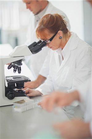 simsearch:6109-08389507,k - Female scientist looking through a microscope standing next to her colleagues Stock Photo - Premium Royalty-Free, Code: 6109-07497739