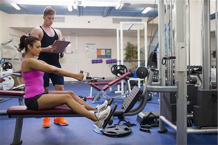 simsearch:6109-07497869,k - Instructor taking notes of woman exercising in weights room of gym Foto de stock - Sin royalties Premium, Código: 6109-07497852