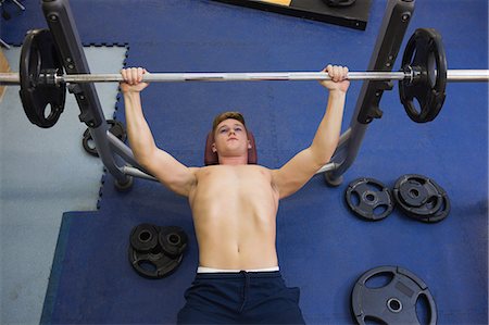 Muscular good looking man lying on bench lifting barbell in weights room of gym Stock Photo - Premium Royalty-Free, Code: 6109-07497899