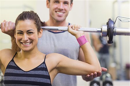 Instructor helping smiling woman lifting barbell in weights room of gym Stock Photo - Premium Royalty-Free, Code: 6109-07497948