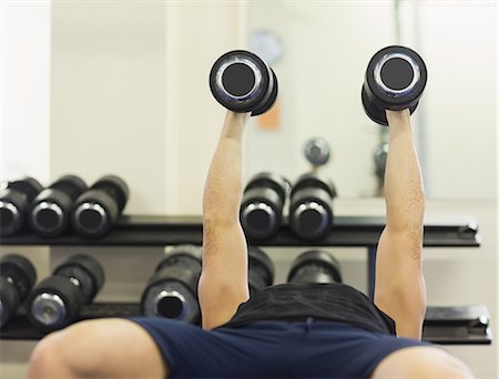 simsearch:6109-07497902,k - Muscular man lying on bench holding dumbbells in weights room of gym Photographie de stock - Premium Libres de Droits, Code: 6109-07497905