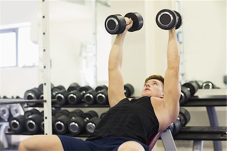 simsearch:6109-07497833,k - Muscular attractive man lying on bench training with dumbbells in weights room of gym Foto de stock - Royalty Free Premium, Número: 6109-07497909