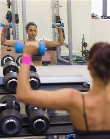 simsearch:6109-07497869,k - Sporty woman lifting dumbbells looking into mirror in weights room of gym Foto de stock - Sin royalties Premium, Código: 6109-07497924