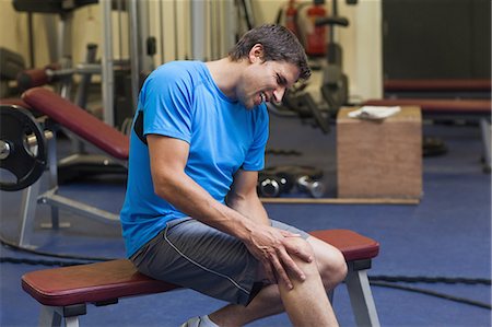 dolorido - Side view of a healthy young man with an injured leg sitting in the gym Foto de stock - Sin royalties Premium, Código: 6109-07498063