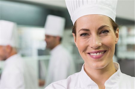 simsearch:6109-07601051,k - Smiling chef looking at camera with team working behind Foto de stock - Sin royalties Premium, Código: 6109-07601050